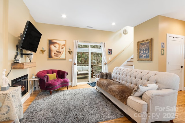 living room featuring stairway, wood finished floors, a glass covered fireplace, visible vents, and recessed lighting