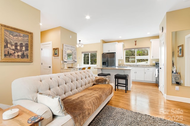 living room with recessed lighting, plenty of natural light, a notable chandelier, and light wood-type flooring