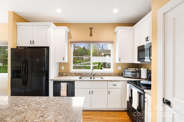 kitchen with light stone countertops, white cabinetry, a sink, and black appliances