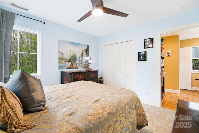 bedroom with a ceiling fan, wood finished floors, a closet, baseboards, and visible vents