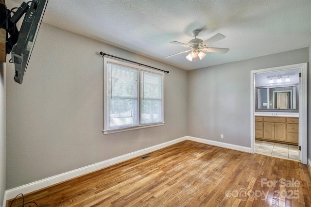 4897 Calico Rd, Lenoir, NC 28645 - unfurnished bedroom featuring light wood finished floors, ensuite bathroom, a textured ceiling, and ceiling fan