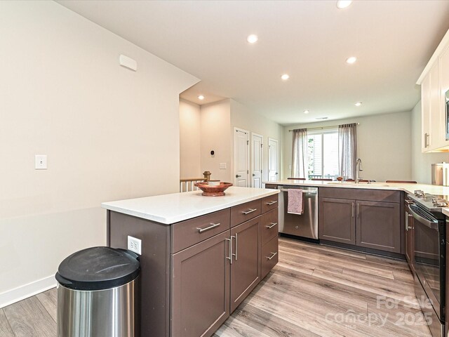 kitchen featuring stainless steel dishwasher, light wood-style flooring, a sink, a peninsula, and black electric range oven