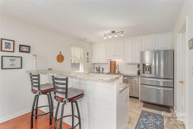 kitchen with a kitchen breakfast bar, appliances with stainless steel finishes, light stone countertops, a sink, and white cabinetry