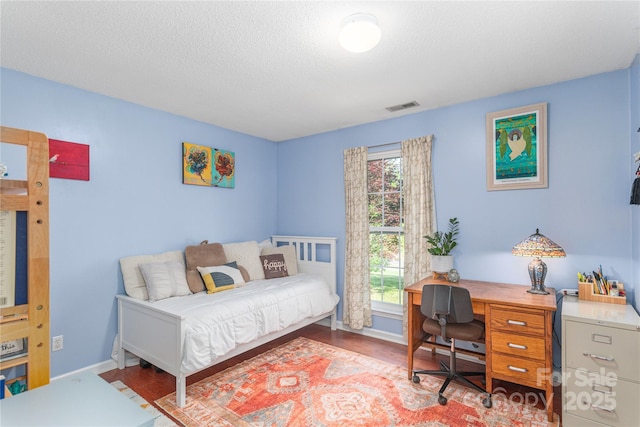 bedroom featuring a textured ceiling, baseboards, visible vents, and wood finished floors