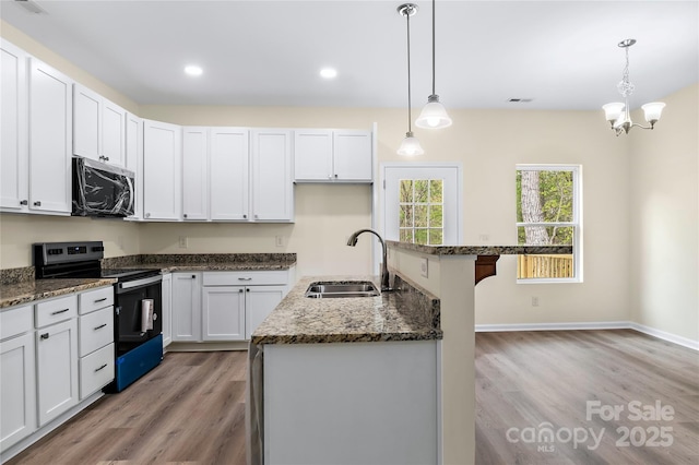 kitchen with decorative light fixtures, a sink, dark stone countertops, stainless steel appliances, and light wood-style flooring