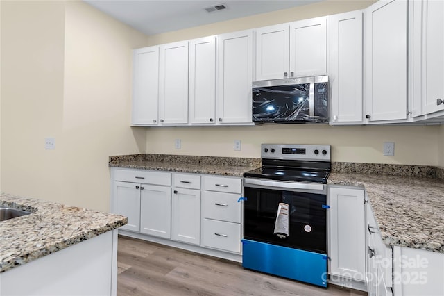 kitchen with appliances with stainless steel finishes, light wood finished floors, light stone counters, and visible vents