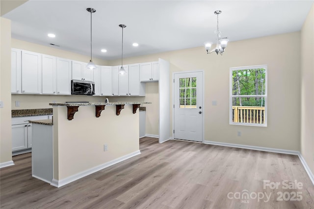 kitchen with an inviting chandelier, light wood-style floors, dark stone countertops, stainless steel microwave, and a kitchen bar