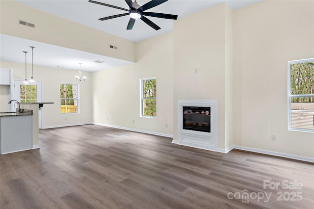 unfurnished living room featuring visible vents, a sink, ceiling fan with notable chandelier, and dark wood-type flooring