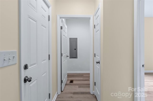 hall with baseboards, visible vents, wood finished floors, and electric panel