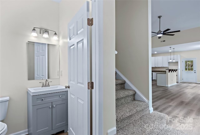 bathroom featuring ceiling fan, wood finished floors, vanity, baseboards, and toilet