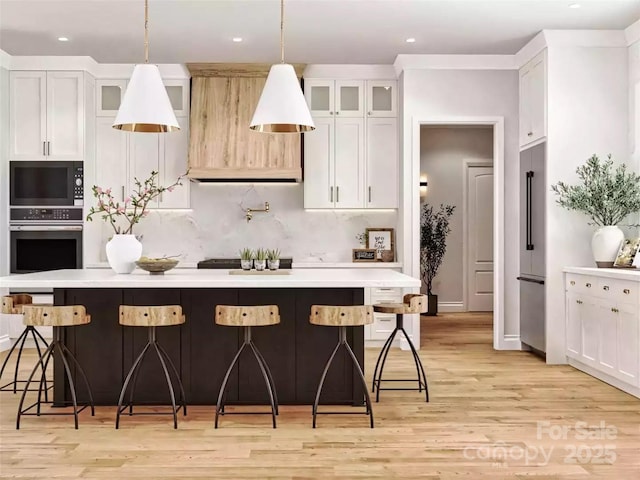 kitchen featuring decorative backsplash, light countertops, black appliances, light wood finished floors, and a center island
