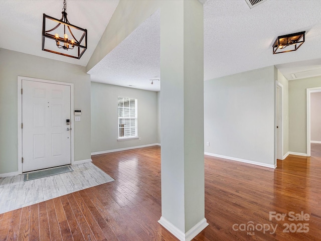 entryway with a textured ceiling, an inviting chandelier, hardwood / wood-style flooring, and baseboards