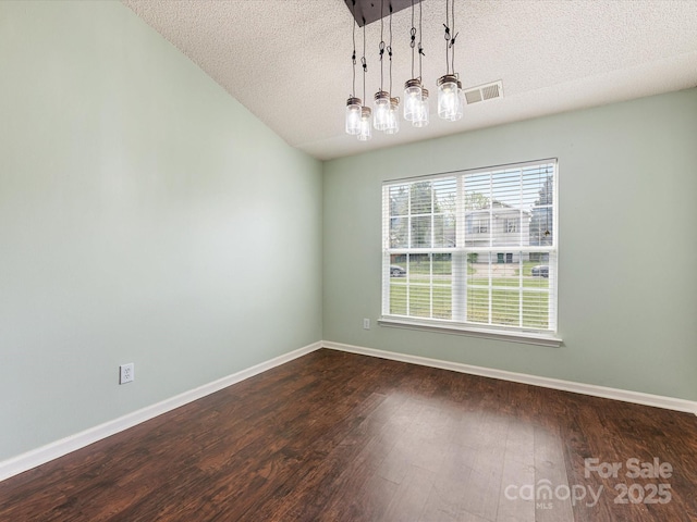 unfurnished dining area with a textured ceiling, visible vents, dark wood-style flooring, and baseboards