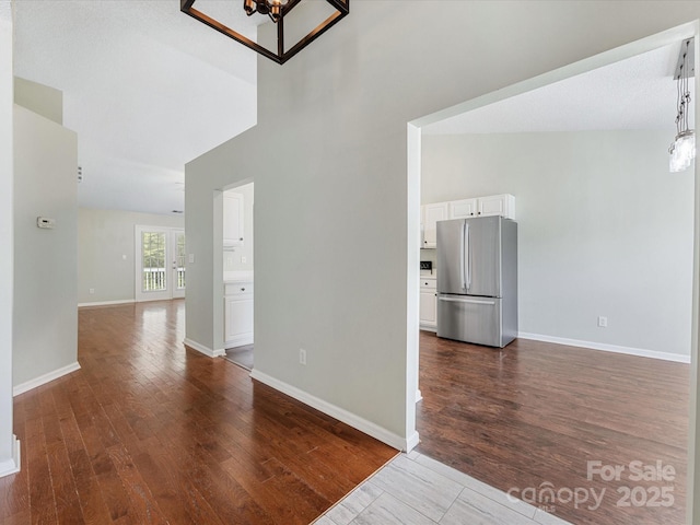 interior space with an inviting chandelier, dark wood-style flooring, a towering ceiling, and baseboards