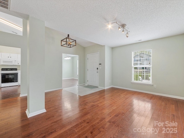 unfurnished living room with visible vents, wood finished floors, an inviting chandelier, and a textured ceiling