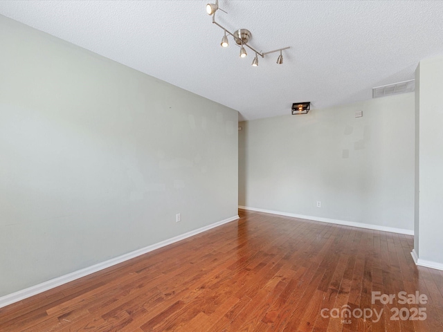 spare room featuring baseboards, visible vents, wood finished floors, and a textured ceiling