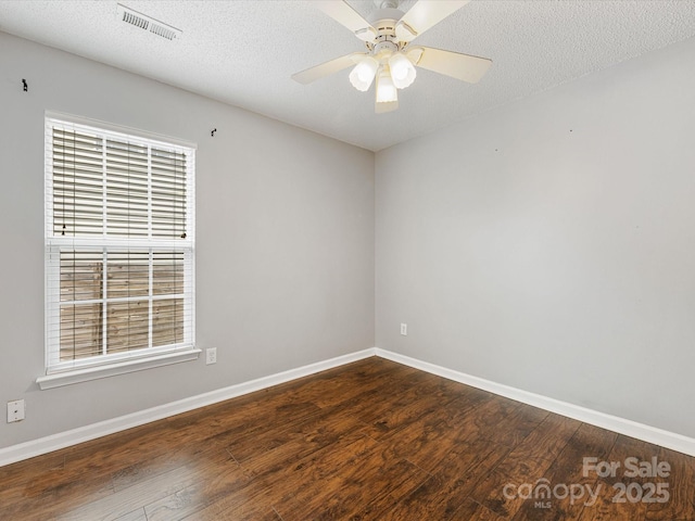 spare room featuring a textured ceiling, visible vents, ceiling fan, baseboards, and dark wood finished floors