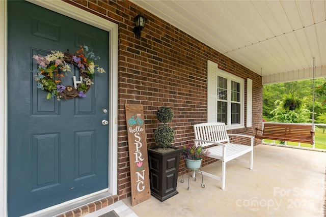 entrance to property with a porch and brick siding