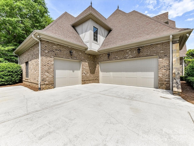 view of side of property featuring brick siding, an attached garage, driveway, and a shingled roof