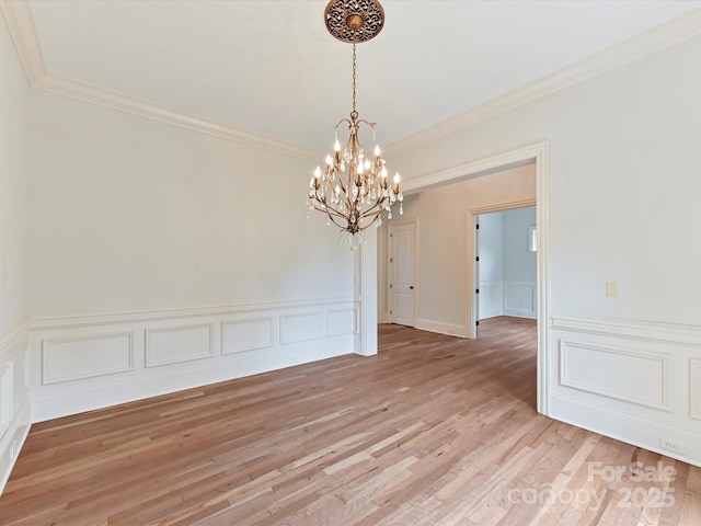 unfurnished dining area featuring light wood-style flooring, a wainscoted wall, a chandelier, crown molding, and a decorative wall