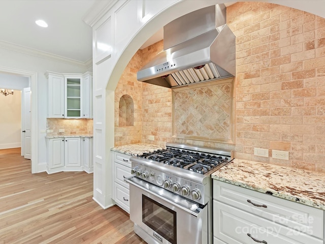 kitchen with light wood finished floors, backsplash, ornamental molding, wall chimney exhaust hood, and stainless steel range