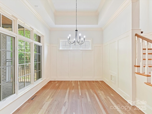unfurnished dining area featuring a decorative wall, stairs, light wood finished floors, a notable chandelier, and visible vents