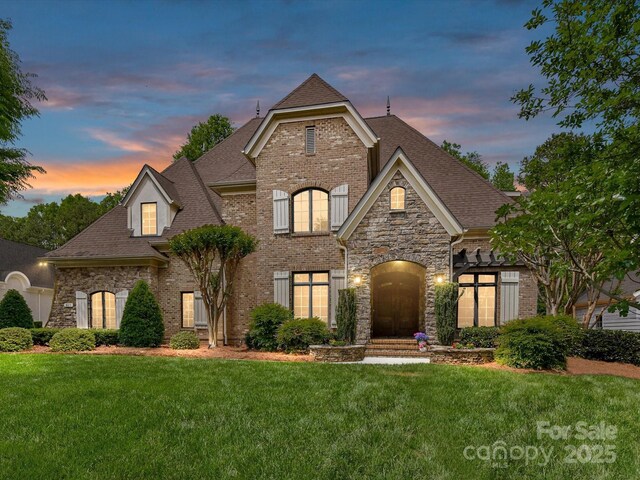 french provincial home featuring stone siding, brick siding, a yard, and a shingled roof