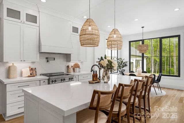 2165 Country Club Rd, Lincolnton, NC 28092 - kitchen with custom exhaust hood, a kitchen island with sink, range, light wood finished floors, and white cabinetry