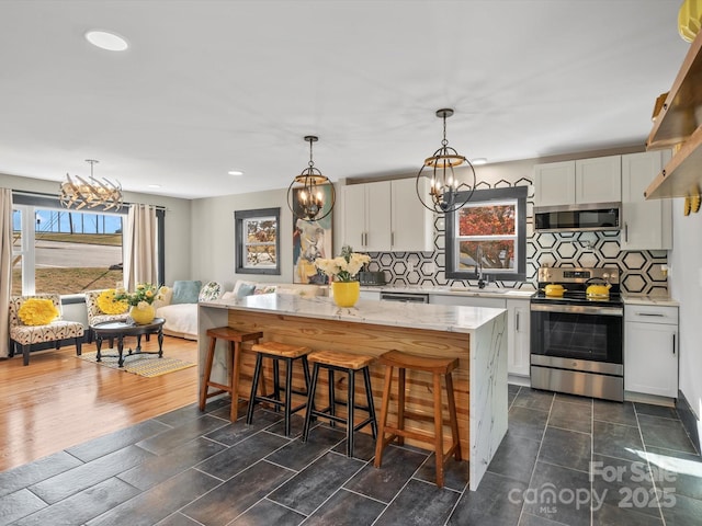 kitchen with a center island, light stone counters, an inviting chandelier, white cabinets, and appliances with stainless steel finishes