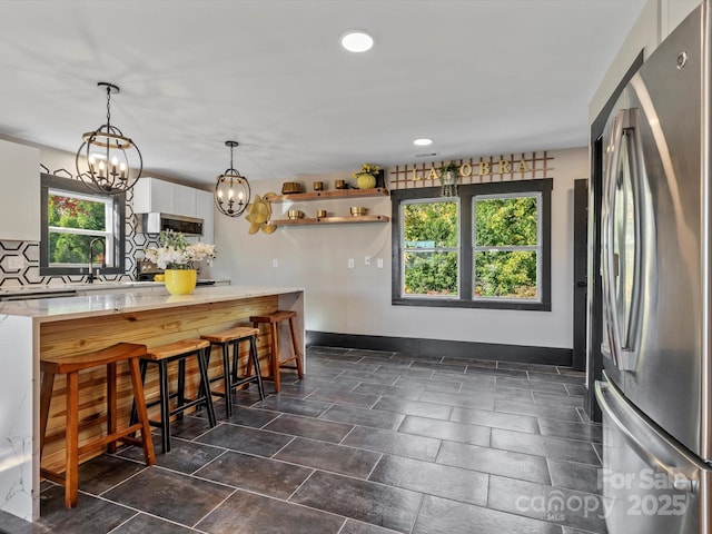 kitchen featuring light countertops, open shelves, freestanding refrigerator, baseboards, and decorative backsplash