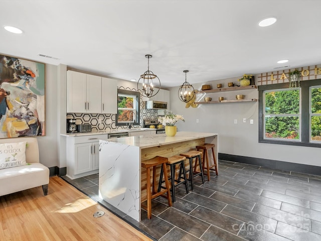 kitchen featuring white cabinets, decorative backsplash, stainless steel microwave, baseboards, and a kitchen island