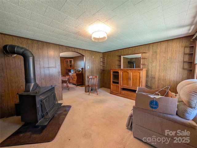 living room with arched walkways, a wood stove, wood walls, and light carpet