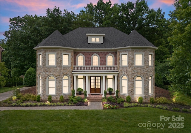 colonial-style house with french doors, a front yard, stone siding, and roof with shingles