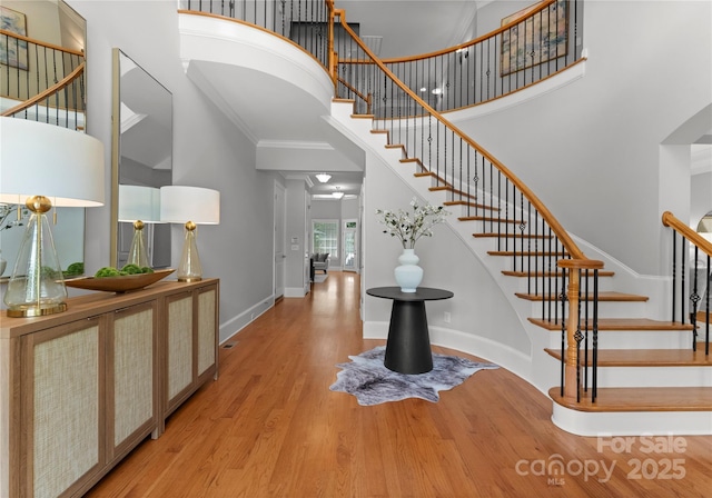 foyer with a high ceiling, wood finished floors, stairway, baseboards, and ornamental molding
