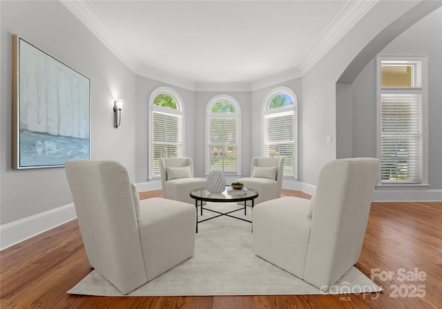 living room with arched walkways, crown molding, baseboards, and wood finished floors