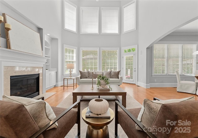 living room featuring built in features, light wood-style flooring, baseboards, a high end fireplace, and a high ceiling