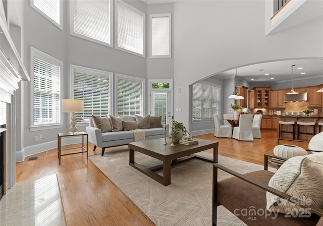 living room featuring arched walkways, a high ceiling, light wood finished floors, crown molding, and baseboards