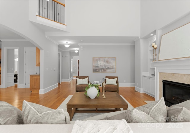 living room featuring ornamental molding, baseboards, light wood finished floors, a high ceiling, and arched walkways