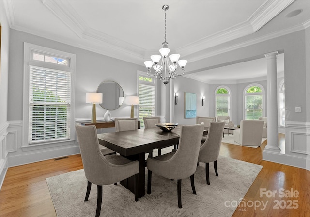 dining area featuring a chandelier, a tray ceiling, crown molding, light wood-style flooring, and wainscoting