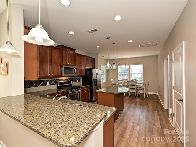 kitchen with stainless steel appliances, backsplash, stone counters, a kitchen island, and visible vents