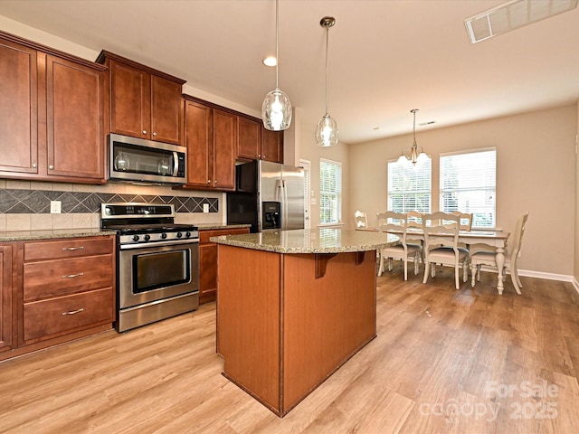 kitchen with light stone countertops, appliances with stainless steel finishes, decorative backsplash, light wood-type flooring, and a kitchen island