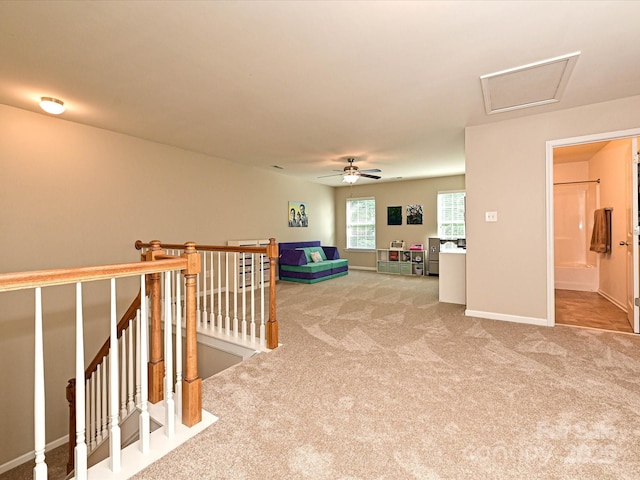 interior space featuring ceiling fan, light carpet, attic access, baseboards, and an upstairs landing