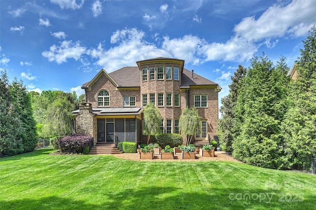 rear view of property with a sunroom, a patio area, a yard, and brick siding