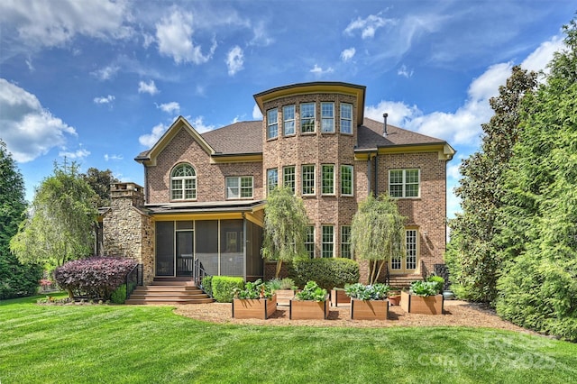 rear view of house with a sunroom, a lawn, a vegetable garden, and brick siding
