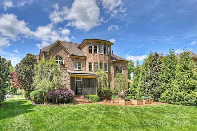 rear view of property featuring a sunroom, fence, a yard, and brick siding