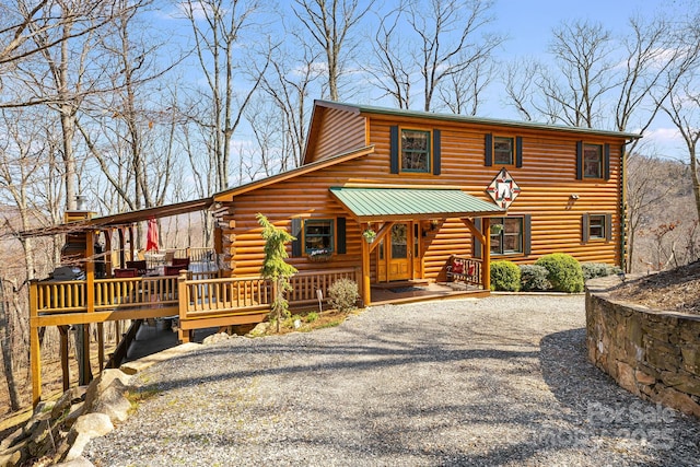 view of front of house with covered porch, gravel driveway, and log exterior