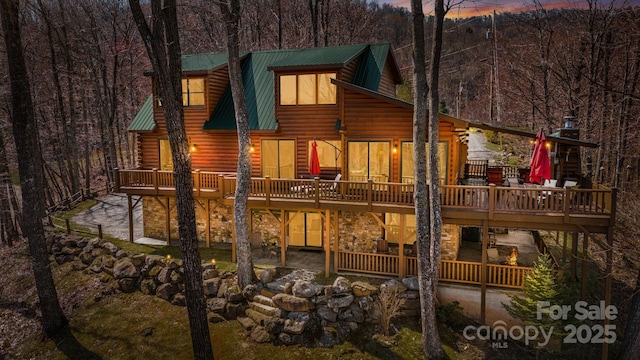 back of property at dusk with metal roof, a wooden deck, stone siding, and log siding