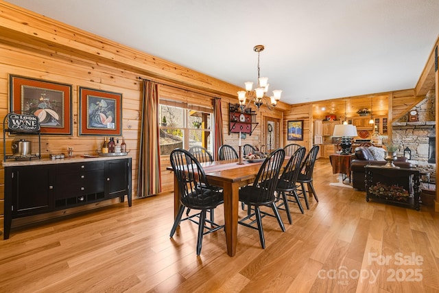 dining space with wood walls, a chandelier, and light wood-style flooring