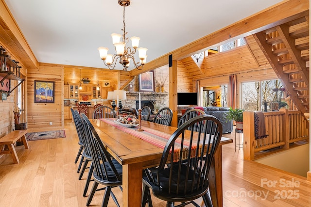 dining area with light wood-style floors, a notable chandelier, wooden walls, and a fireplace