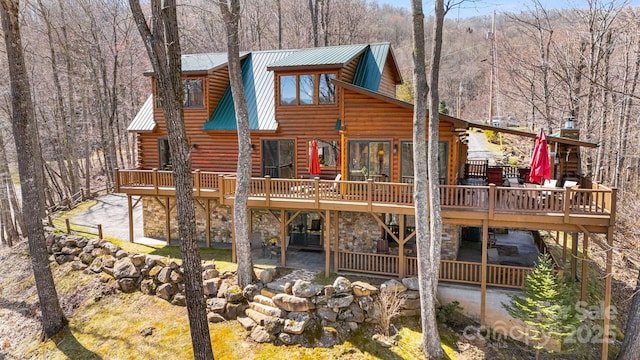 rear view of house featuring metal roof, a deck, stone siding, and log exterior